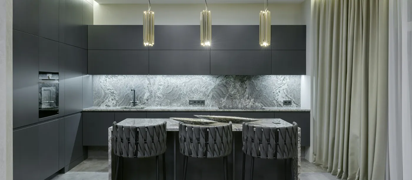 A graphite kitchen with slab doors, a marble backsplash, a waterfall island with three woven stools and three brass pendants.