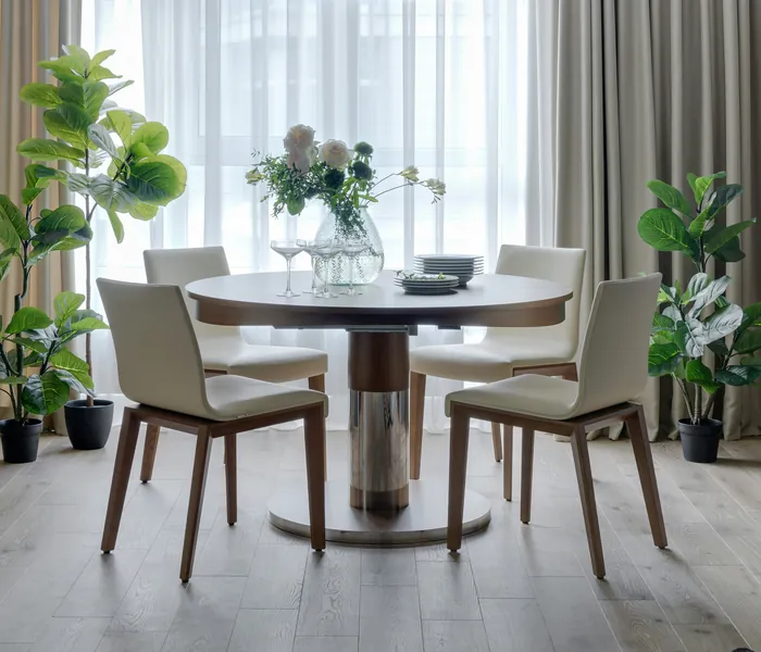 The dining corner of our showroom: a round walnut table with four cream chairs in front of sheer curtains.