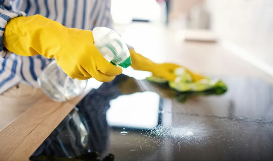Gloved hands spraying and wiping a black glass stovetop