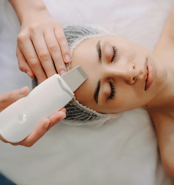 An esthetician guiding an ultrasonic cleansing wand across a client's forehead