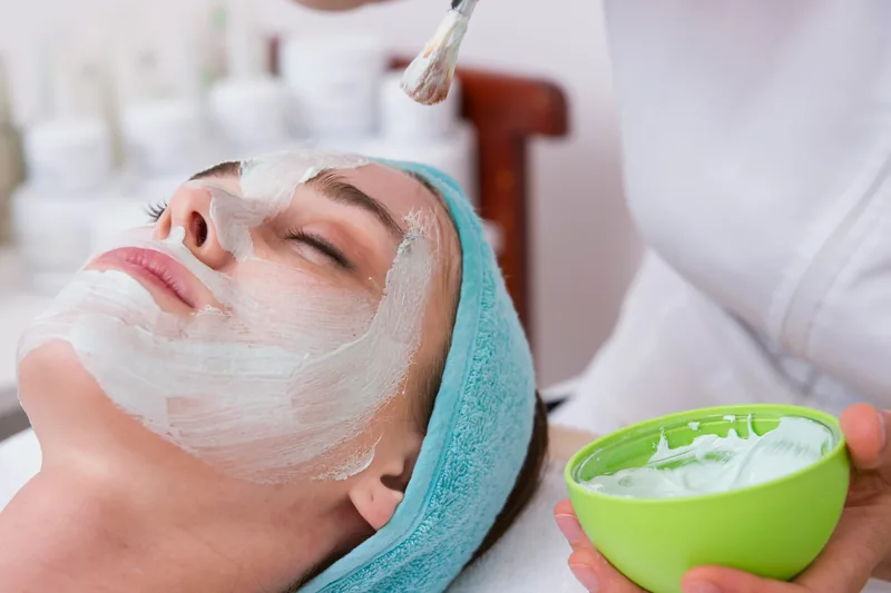A hydrating mask being brushed onto a client's face, the bowl of mask in the esthetician's hand