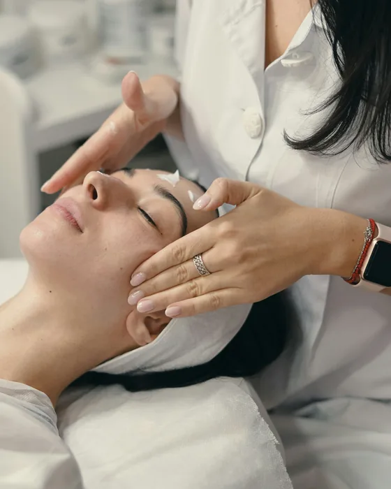 An esthetician in a white coat massaging cream into a client's forehead and temples
