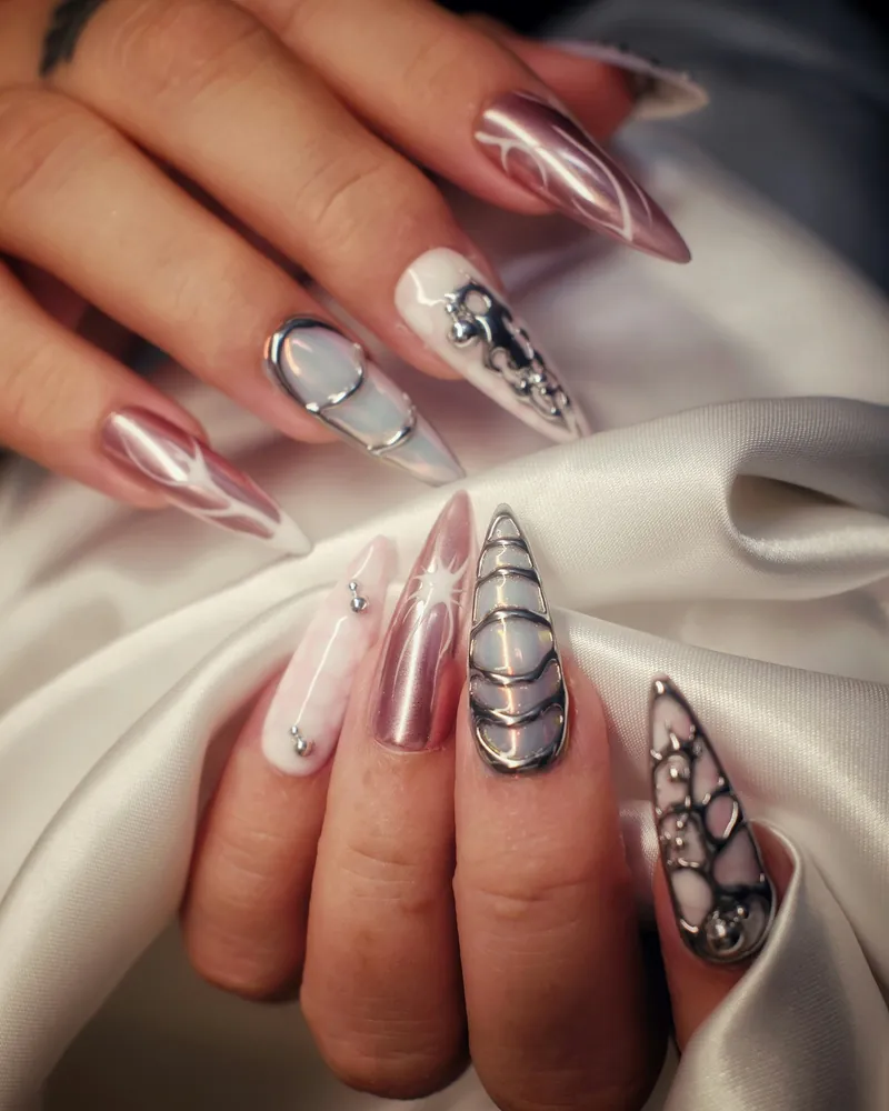 Long stiletto nails in rose chrome and milk white with raised silver lines and small crystals, held against white satin