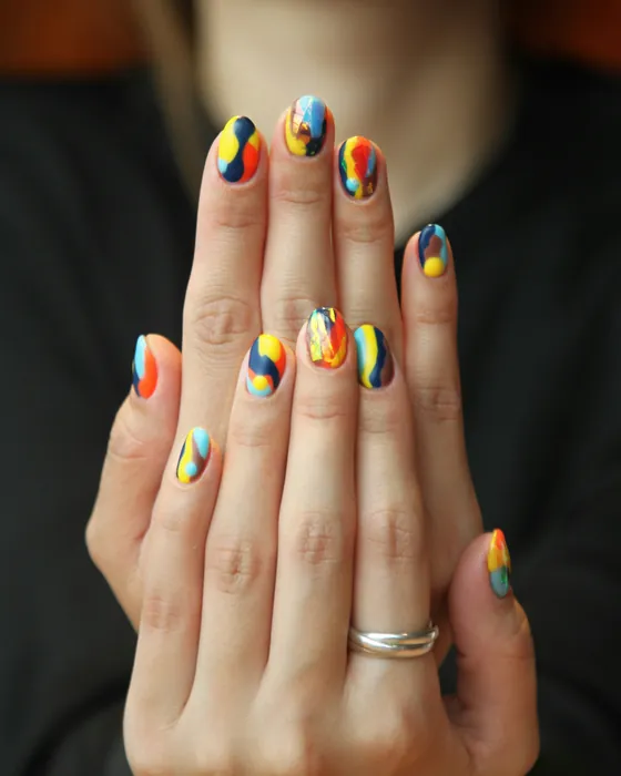 Two hands held up, short round nails each painted with an abstract design in navy, yellow, orange and sky blue