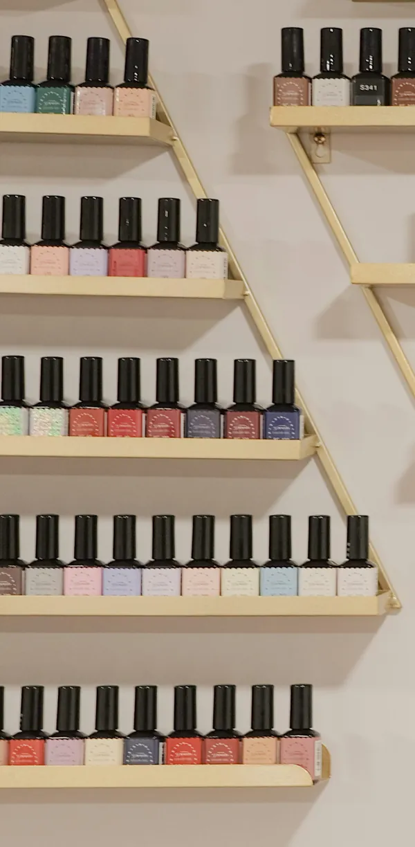 Rows of gel polish bottles in nudes, pinks, reds and blues on brass wall shelves