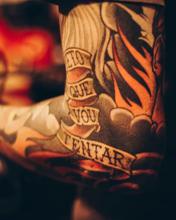 A lettering banner wrapped through orange flames on an upper arm