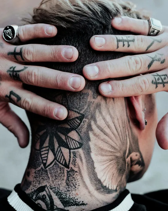 Small black symbols tattooed along the fingers, a dotwork flower on the neck behind them