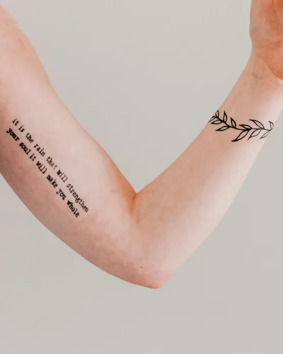 A thin olive sprig around a wrist and a line of typewriter script on the forearm