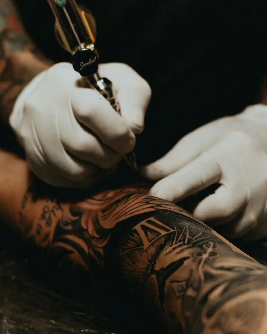 Gloved hands shading a black-and-grey forearm sleeve