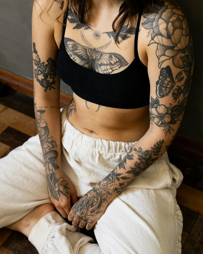 A client sitting cross-legged, a moth tattooed across her chest and two full sleeves