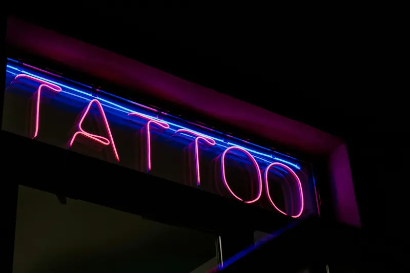 A pink and blue neon tattoo sign glowing over the door at night
